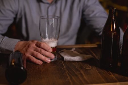 Foto colorida: homem segura copo de cerveja pela metade - Metrópoles