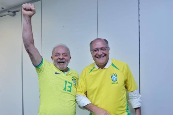 Os presidente e vice eleitos, respectivamente, Lula e Alckmin comemoram vitória do Brasil contra Suíça em copa do mundo do Catar. Eles sorriem, usando camisas do Brasil, e Lula ergue a mão - Metrópoles