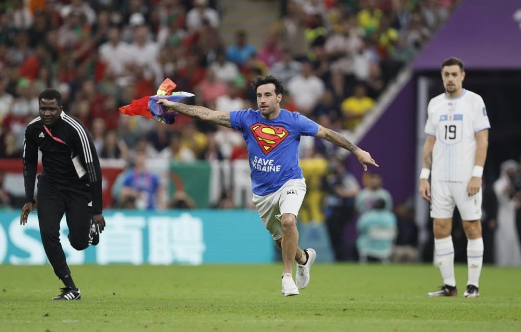 Torcedor segurando uma bandeira LGBTQIA+ dentro de um campo durante jogo no Catar