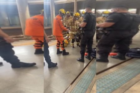 Bombeiros militares e segurança do metrô atendem passageiro marrado em maca no chão. Foto colorida