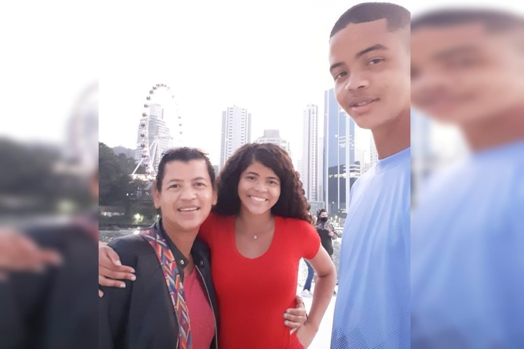 Foto de uma mulher com os filhos na roda com prédios e uma roda gigante atrás