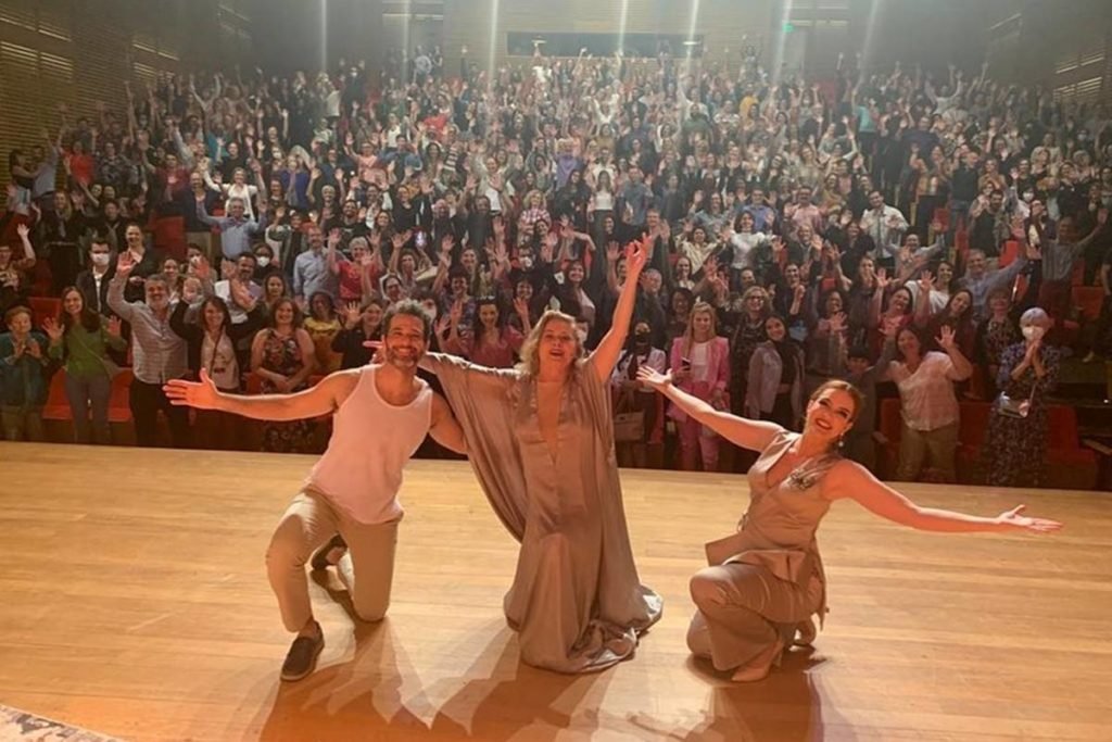homem e duas mulheres de joelhos em palco com plateia animada ao fundo - metrópoles