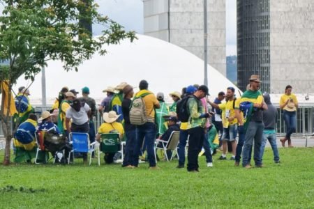 Grupo de pessoas trajadas com roupas nas cores da bandeira do Brasil e camisetas amarelas, em gramado em frente ao Congresso Nacional, em Brasília - Metrópoles