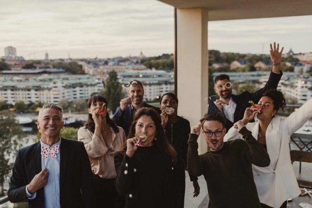 Homens e mulheres de diferentes idades e raças em uma confraternização de trabalho. Eles estão em uma sala com um fundo espelhado, onde é possível ter uma vista panorâmica da cidade. - Metrópoles