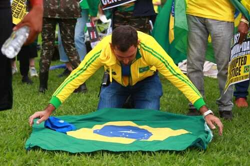 Manifestantes bolsonaristas participam de protesto golpista em frente ao QG do Exército, em Brasília, pedindo intervenção militar. Um deles ajeita uma bandeira do Brasil no chão - Metrópoles