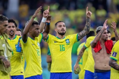 O jogador Alex Telles, em destaque, em meio a outros jogadores a da seleção brasileira após jogo na Copa do Mundo do Catar. Eles erguem a mão para cima agradecendo a vitória - Metrópoles