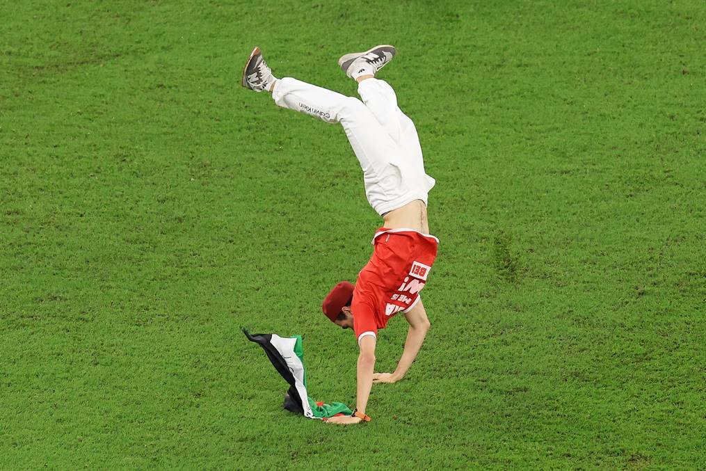 Torcedor invade campo de jogo entre Tunísia e França com uma bandeira da Palestina e seguranças o retiram carregado. No destaque, ele dá uma pirueta no campo - Metrópoles