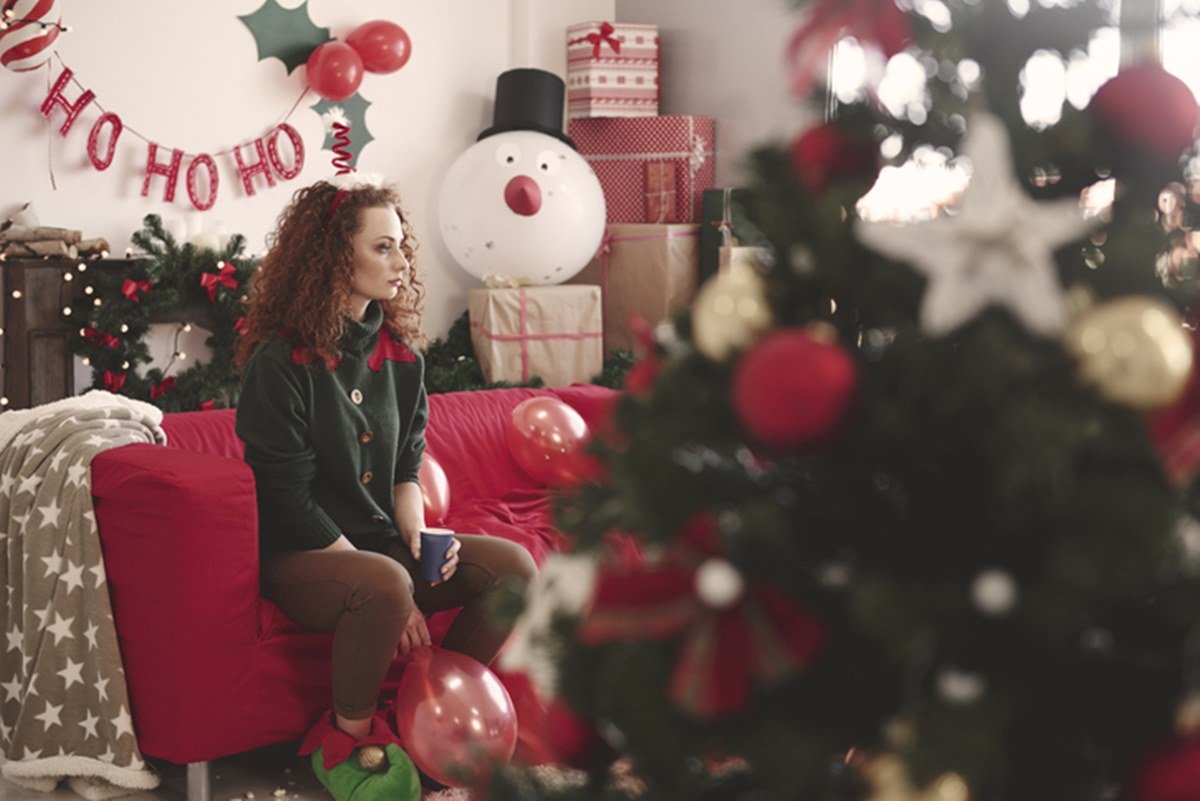 Imagem colorida: sala com decoração de Natal e mulher sentada em sofá olhando para o lado - Metrópoles