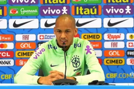 Jogador do Brasil durante entrevista para imprensa. Ele aparece sentado e atrás de um microfone enquanto responde perguntas