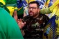 O jornalista bolsonarista Oswaldo Eustáquio conversa com militantes em frente ao QG do Exército trajado com roupas militares. Ele está em cadeira de rodas - Metrópoles