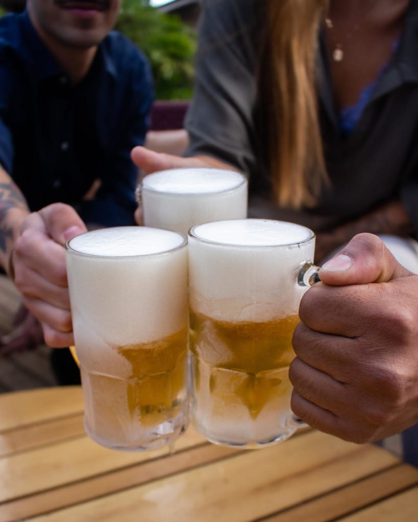 Na foto, três pessoas brindam com canecas de chope - Metrópoles