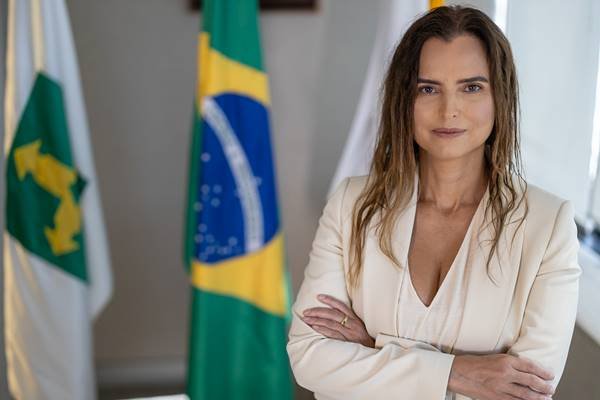 Fotografia colorida de mulher com braços cruzados e bandeiras ao fundo