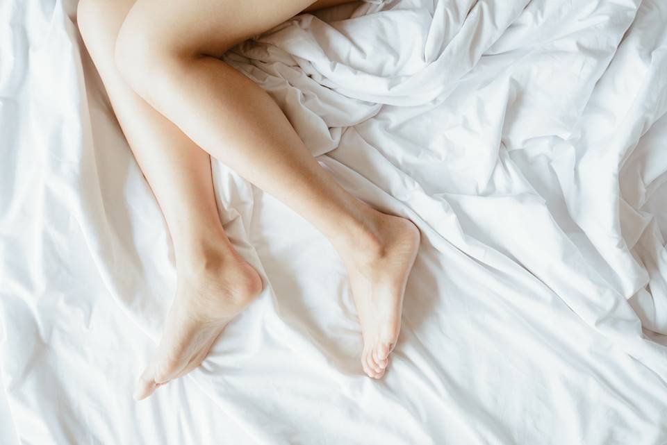 Close de pernas femininas deitadas na cama com lençol branco - Metrópoles