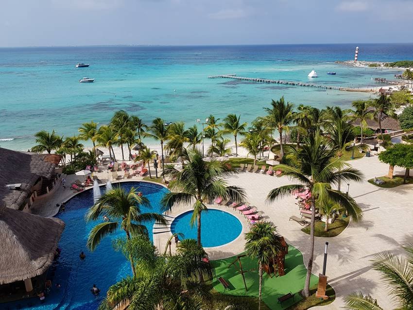 Foto colorida de resort com piscina, mar e coqueiros em Cancún