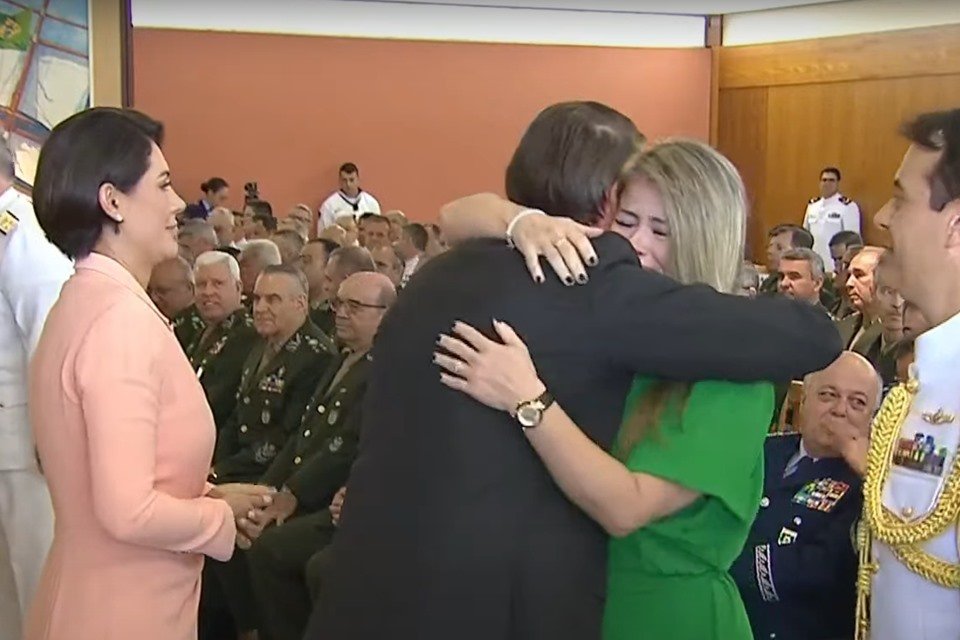 Imagem colorida mostra o presidente Jair Bolsonaro, de costas, abraçando uma mulher vestida de verde - Metrópoles