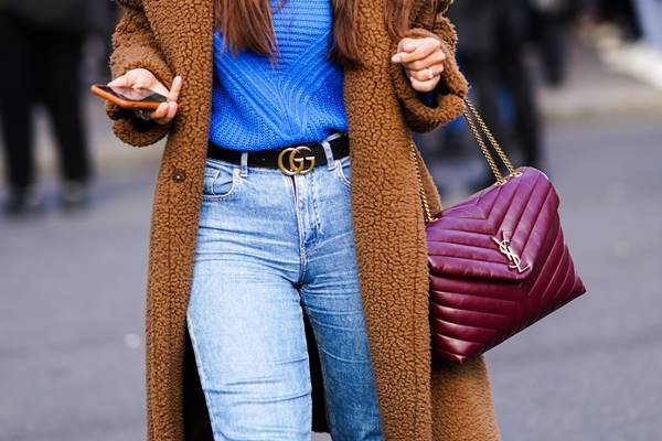 No street style, bolsa magenta da Saint Laurent, em look com calça jeans, blusa azul, sobretudo marrom felpudo e cinto preto com logo da Gucci - Metrópoles
