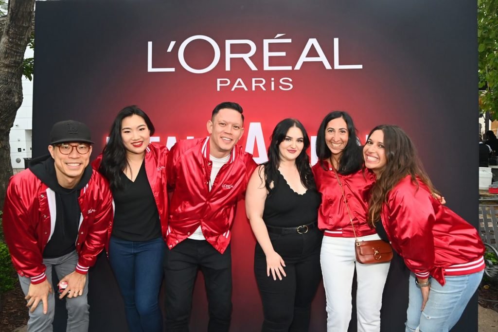 Foto colorida de grupo de pessoas brancas em um evento da L'Óreal. Elas usam casaco vermelho - Metrópoles
