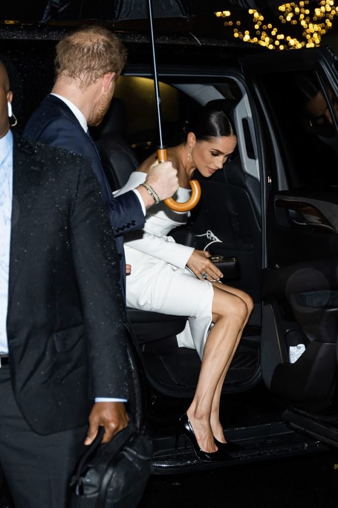 Foto colorida de homem ruivo de terno segurando um guarda-chuva enquanto uma mulher parda com vestido branco sai de um carro - Metrópoles
