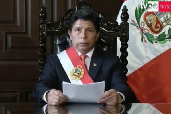 Presidente do Peru, Pedro Castillo, durante pronunciamento de dissolução do Congresso. Ele aparece sentado, segurando um discurso e com a bandeira do Brasil atrás - Metrópoles