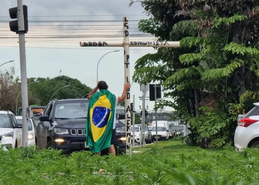 Imagem colorida de bolsonarista se manifestando na W3 Norte com cruz