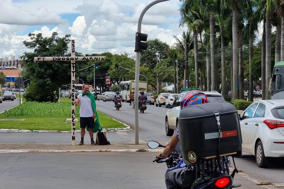 Imagem colorida de bolsonarista se manifestando na W3 Norte com cruz