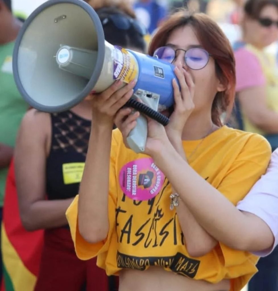 Menina com camisa amarela falando em megafone