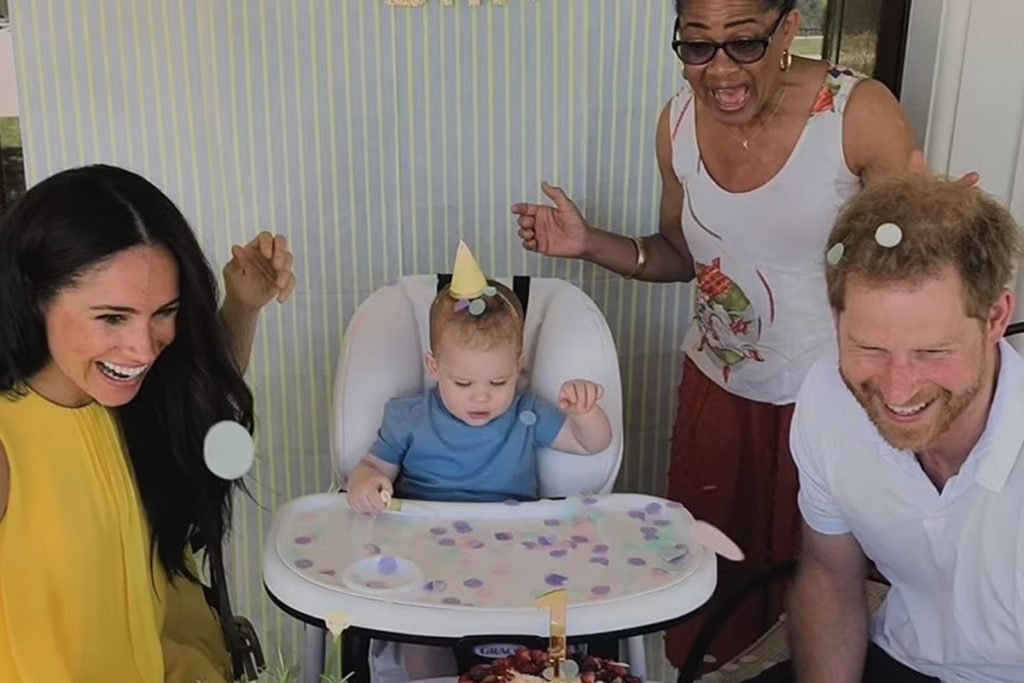 Foto colorida de festa de aniversário de um menino branco, com chapéu amarelo.  Ao lado, duas mulheres negras e um homem branco e ruivo - Metrópoles