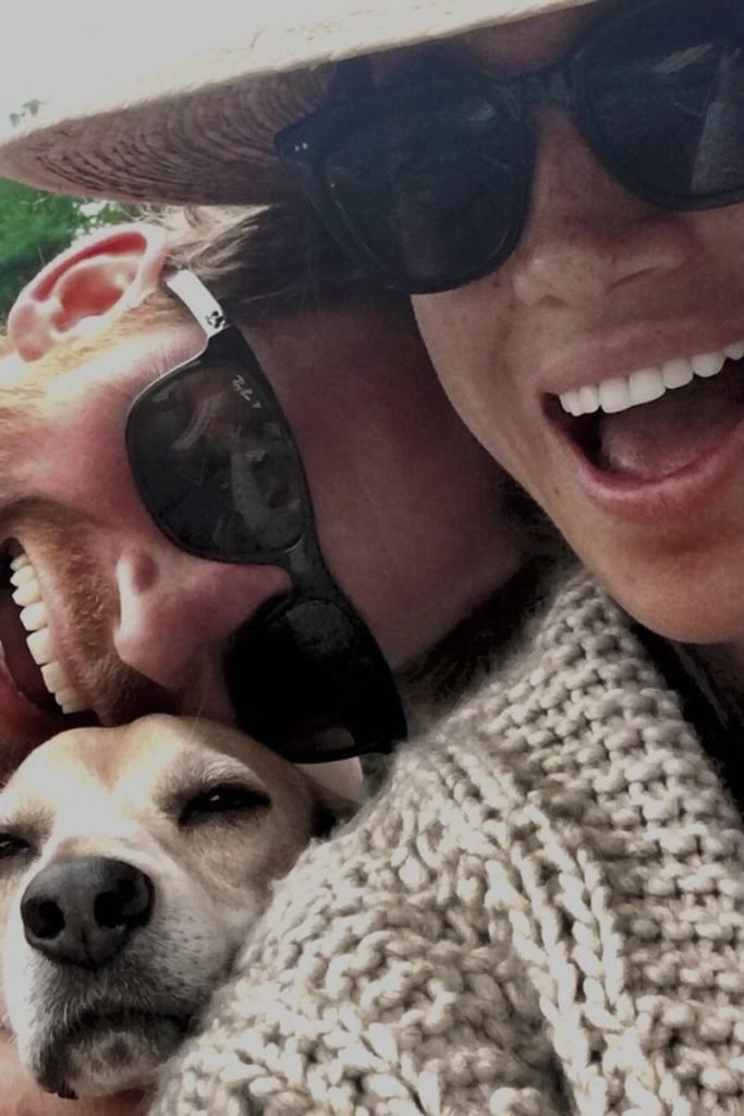 Foto colorida de homem e mulher ao lado de cachorro. O casal está de óculos e sorridente