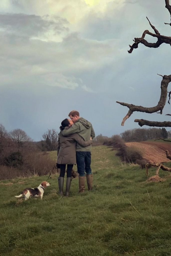 Foto colorida de casal se beijando em uma paisagem de campo. A mulher segura a coleira de um cachorro - Metrópoles