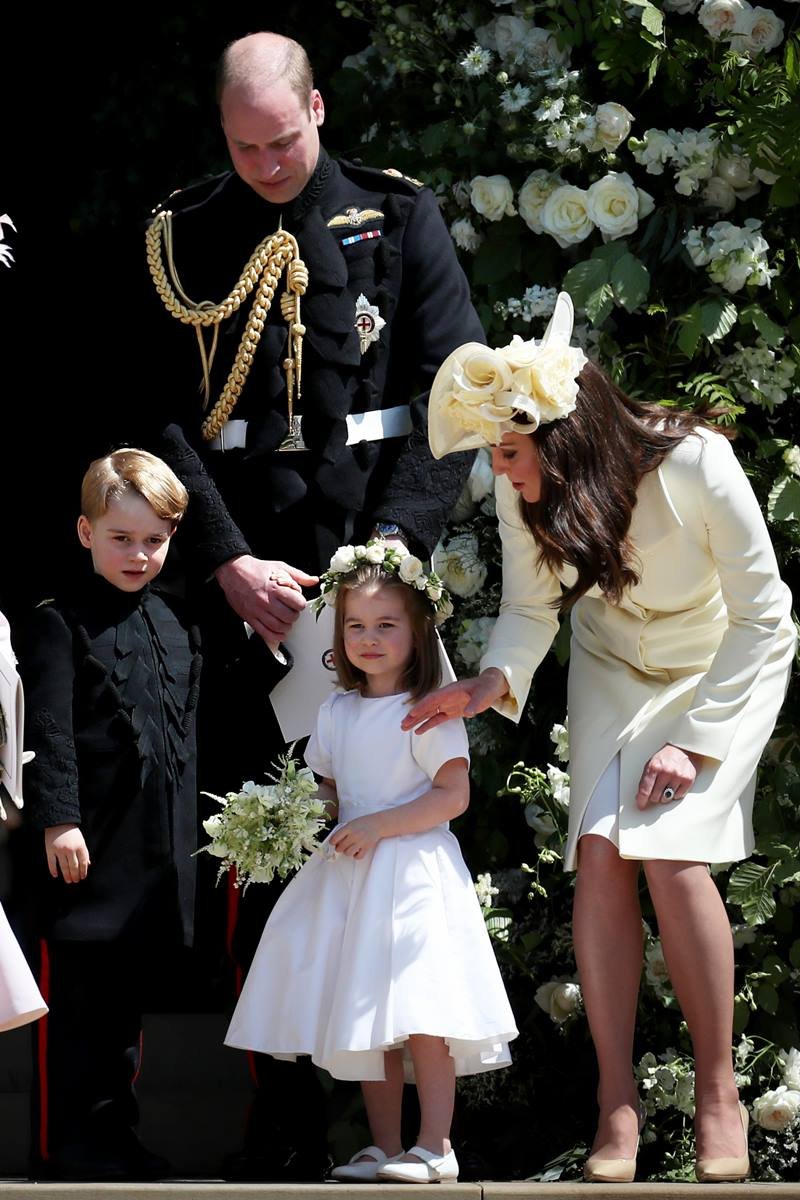 Foto colorida de homem e menino com trajes militares ao lado de menina vestida de dama de honra. Uma mulher está inclinada para falar com a menina - Metrópoles