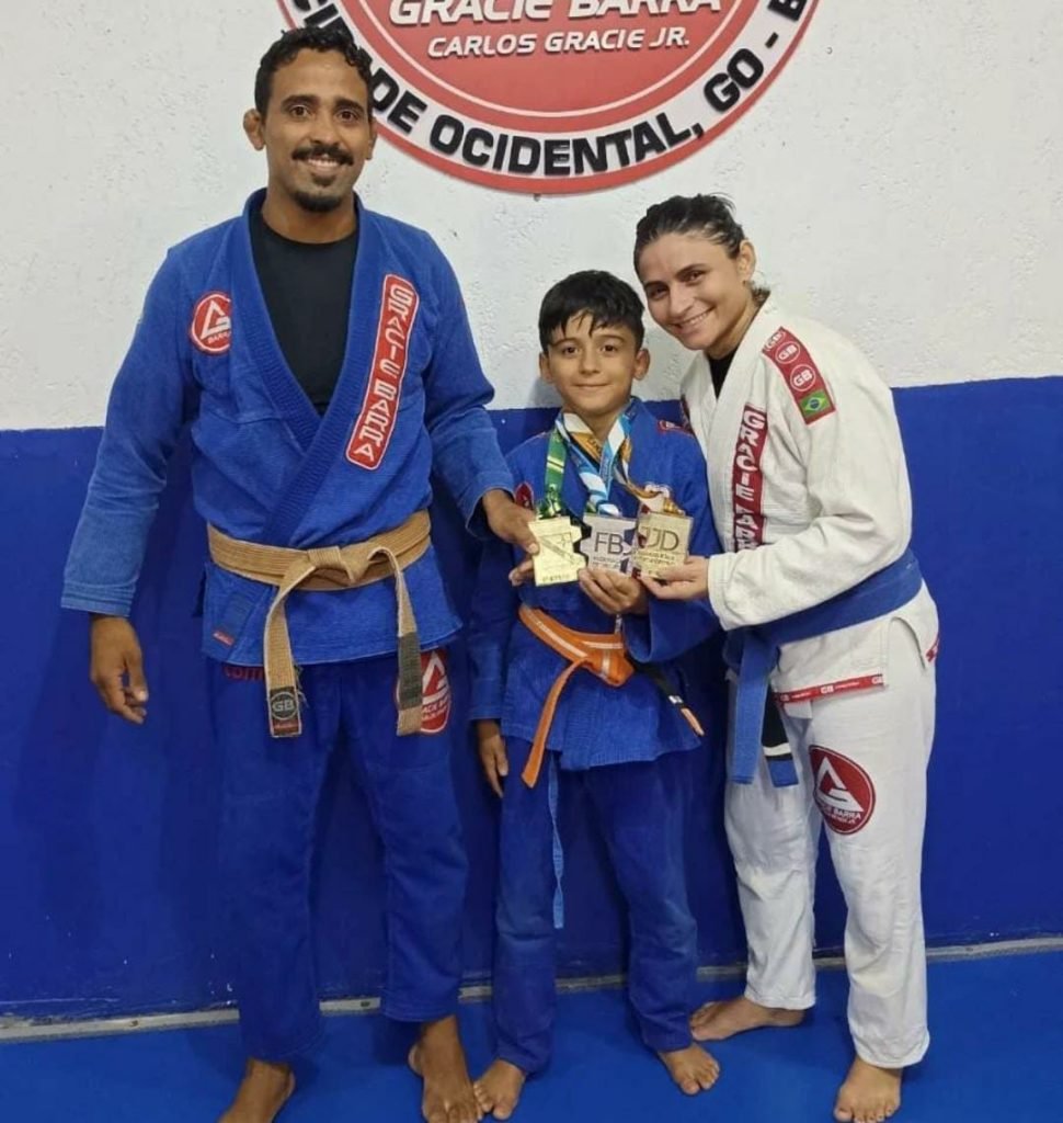 Homem, mulher e menino, abraçados com roupão de luta em tatame