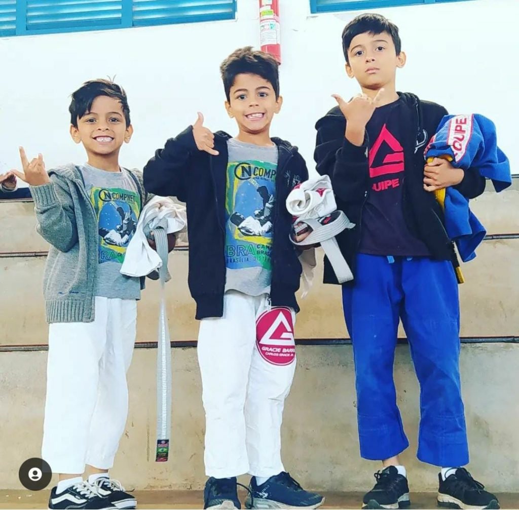 Três meninos pequenos segurando roupão de luta nas mãos e sorrindo