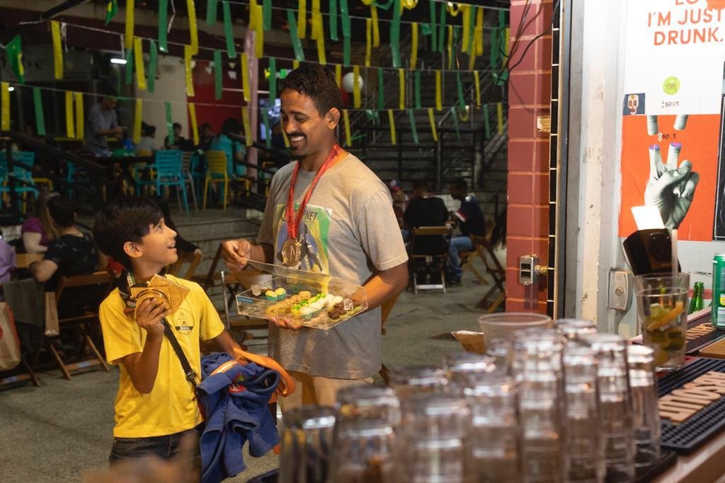 Homem com bandeja de doces na mão olhando para baixo, para menino com camisa amarela