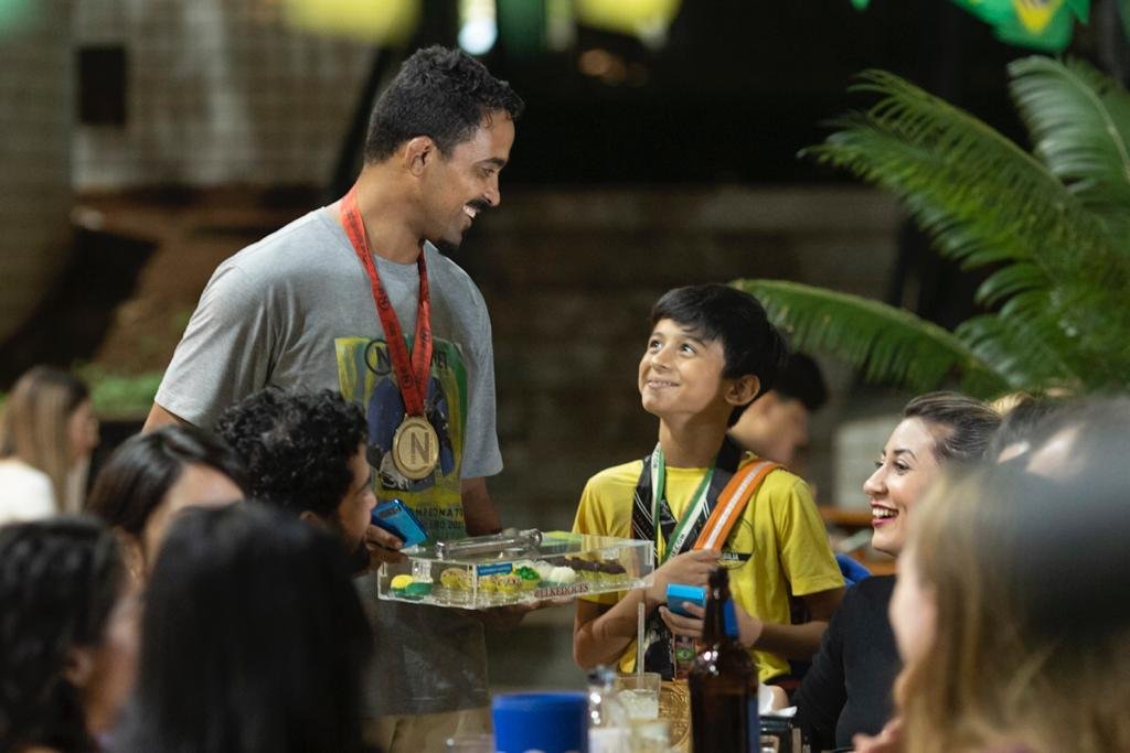 Homem com bandeja de doces na mão olhando para baixo, para menino com camisa amarela