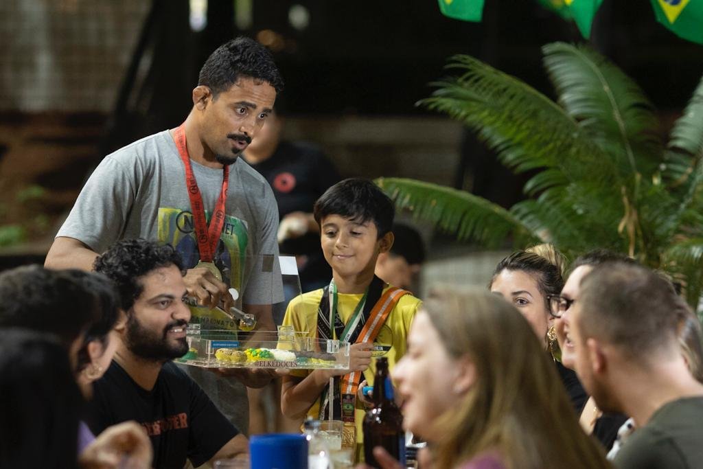 Homem com medalha no pescoço vende brigadeiros para clientes em bar