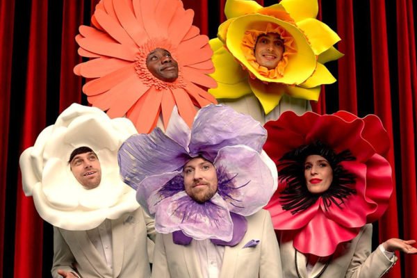 Integrantes da banda inglesa Metronomy com flores gigantes na cabeça - Metrópoles