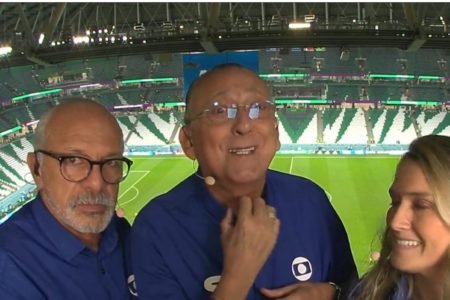 O narrador Galvão Bueno antes de narração de jogo na Copa do Mundo do Catar cercado de dois colegas pela TV Globo - Metrópoles