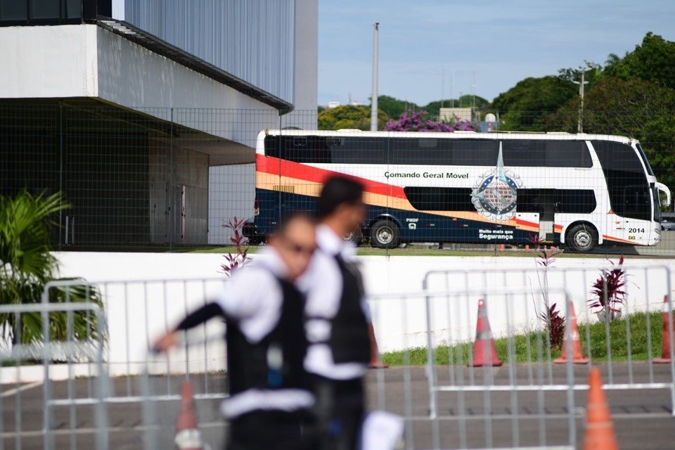 Ônibus da PMDF ao fundo, com dois seguranças uniformizados, cones e grades em primeiro plano, desfocados - Metrópoles