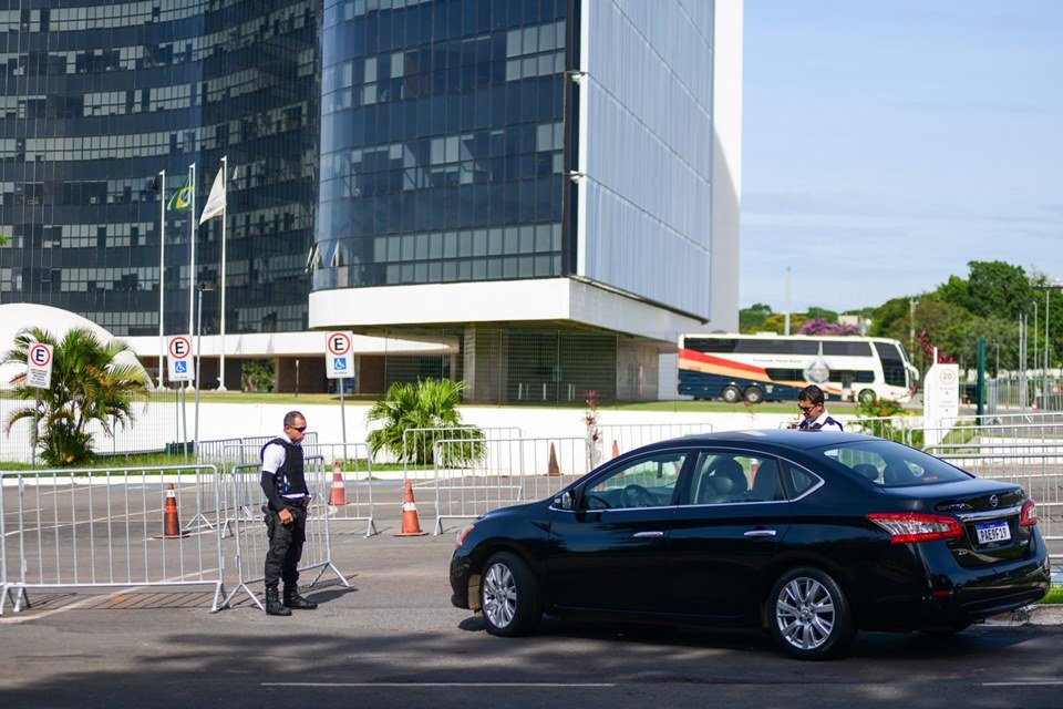 Carro preto parado no estacionamento do TSE, que está com cones e grades, por motivo de segurança. Ao fundo, um ônibus da PMDF. Dois seguranças uniformizados estão posicionados próximo ao veículo - Metrópoles