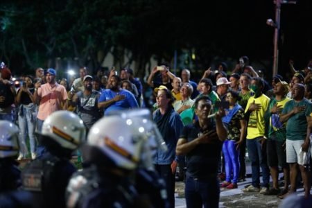 Bolsonaristas promovem caos e destruição no centro de Brasília, na altura da W3 Norte. Na imagem, eles aparecem em pé, cantando o hino nacional no meio de uma pista na frente de agentes da PMDF - Metrópoles