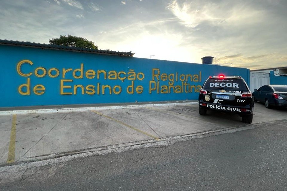 Veículo da Decor, da PCDF, estacionado em frente à sede da Coordenação Regional de Ensino de Planaltina, ao lado de carro preto, estacionado em frente a portão branco da entrada