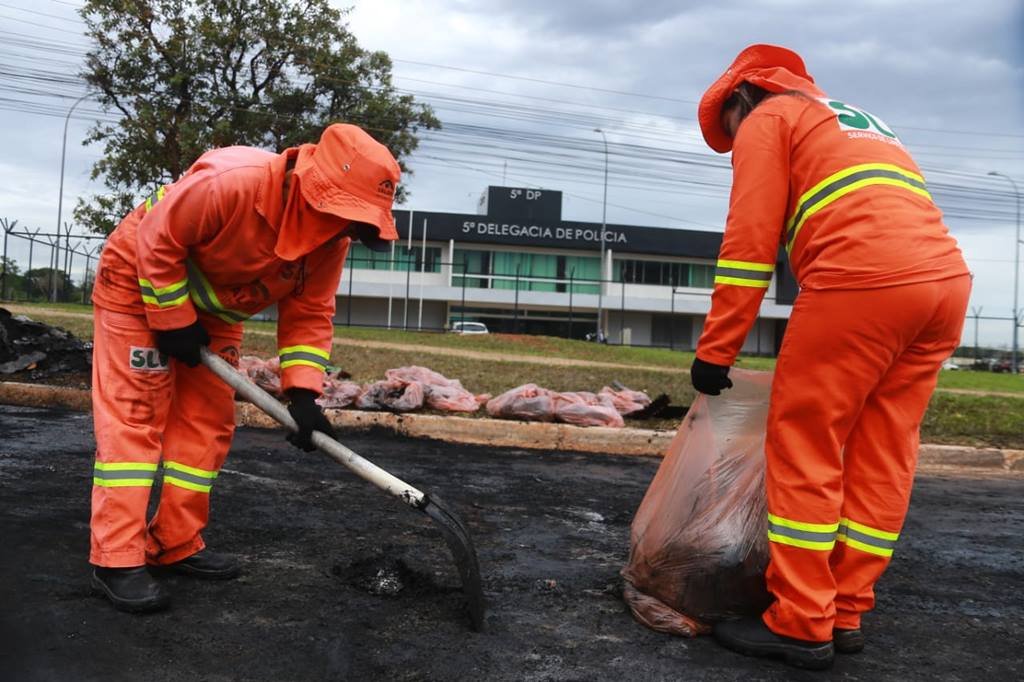 Servidores do SLU fazem a limpeza de asfalto queimado após manifestações de bolsonaristas na Asa Norte do dia de ontem. Na imagem, dois garis limpam local próxima à 5º Delegacia de Polícia Civil do DF - Metrópoles