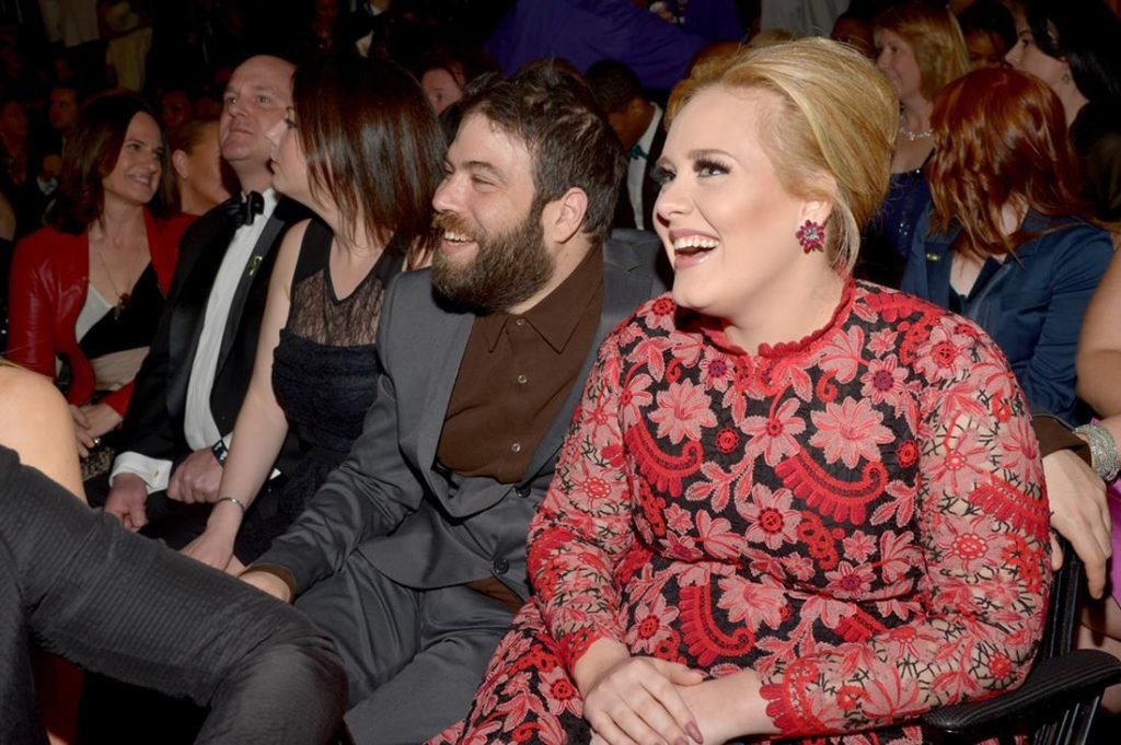 A cantora Adele e seu ex-marido Rich Paul em 2013 em uma premiação musical. Ambos são jovens, brancos e britânicos. Ele usa blazer e calça cinzas e ela usa um vestido florido rosa e vermelho. - Metrópoles