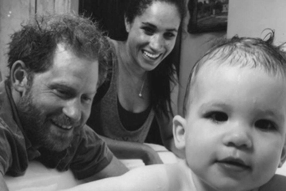 Foto em preto e branco bebê acompanhado de homem e mulher ao fundo sorridentes - Metrópoles