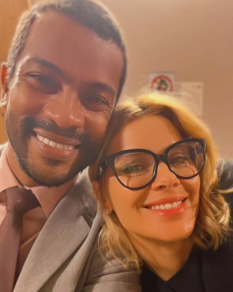 um homem preto e uma mulher loira posam para foto sorrindo - metrópoles