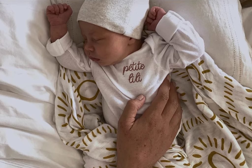 Foto colorida de bebê com mão de um adulto em sua barriga - Metrópoles
