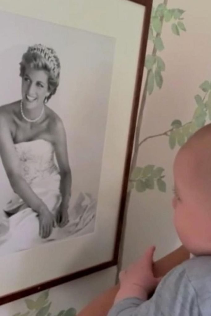 Foto colorida de bebê olhando quadro com uma fotografia de mulher com tiara na cabeça - Metrópoles