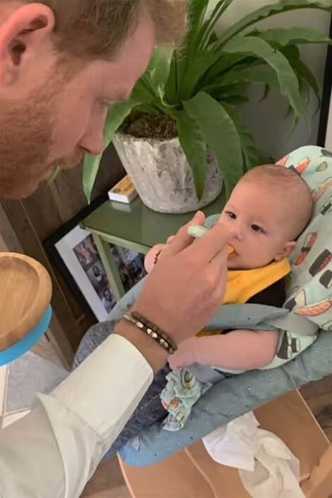 Foto colorida de homem branco e ruivo dando comida na boca para um bebê sentado em uma cadeira infantil - Metrópoles