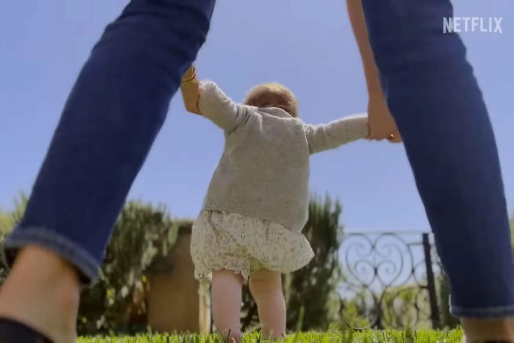Foto colorida de bebê branca e ruiva andando sendo segurada por mãos de mulher - Metrópoles