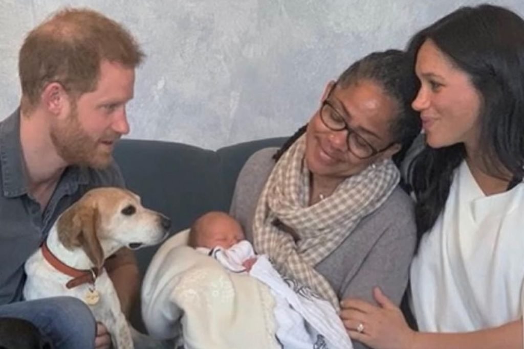 Foto colorida de homem ruivo e branco com um cachorro da raça beagle no colo ao lado de mulher negra com bebê no colo e mulher parda sorridente - Metrópoles